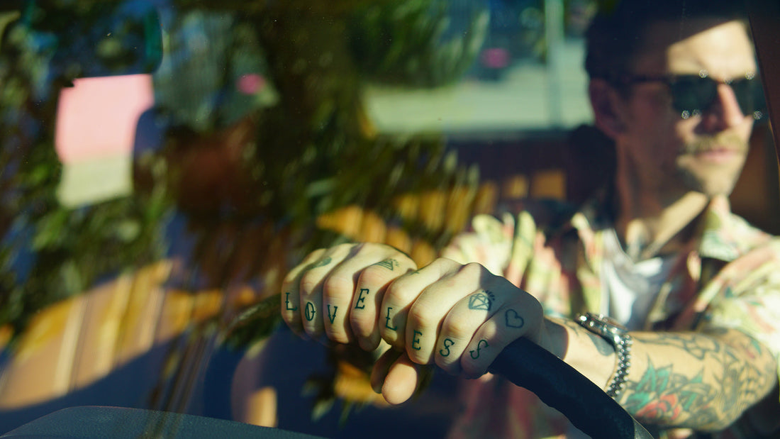 Man with tattoos driving a car, reflected in the window