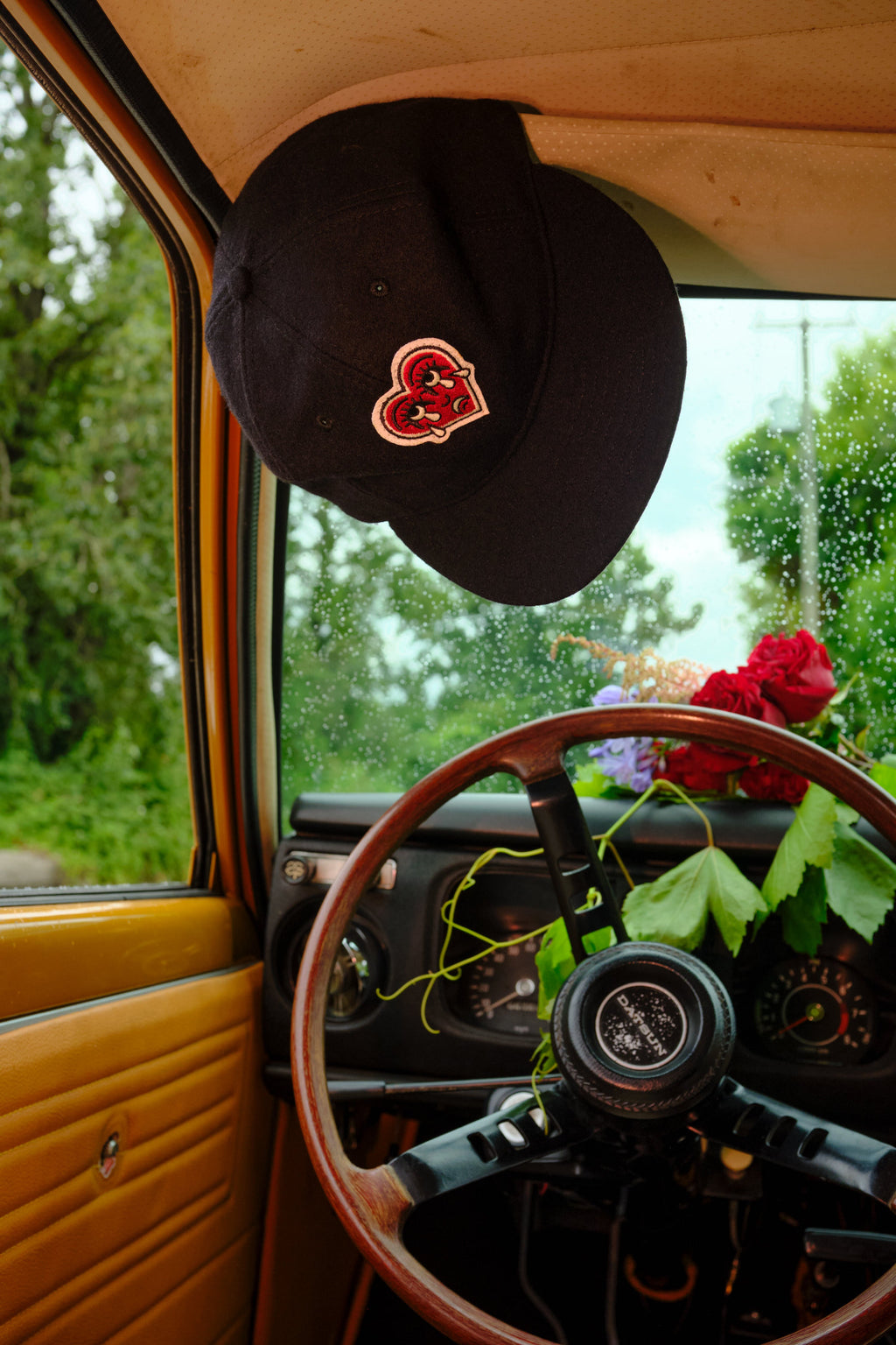 Black cap with a crying heart logo patch on a car dashboard with flowers and steering wheel visible