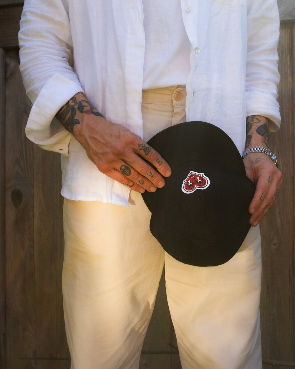Person holding a black cap with a crying heart logo patch against a wooden background
