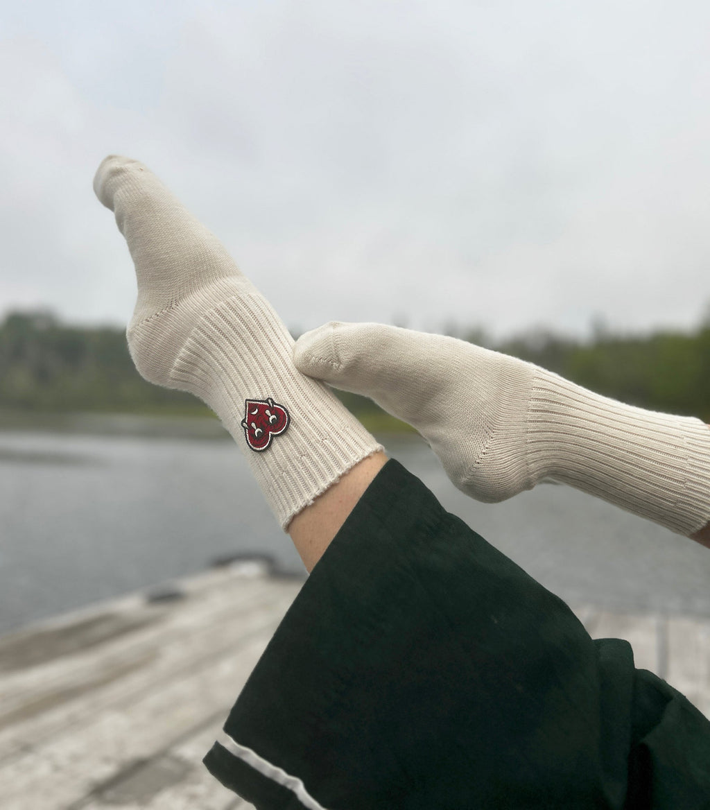 Natural wool socks with a red crying heart logo worn by a person against a blurred natural background