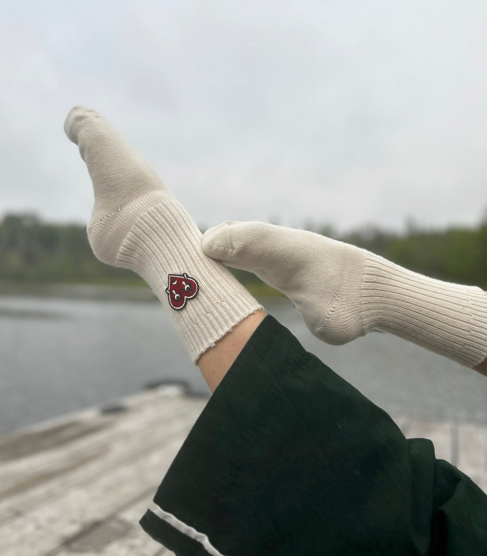 Natural wool socks with a red crying heart logo worn by a person against a blurred natural background